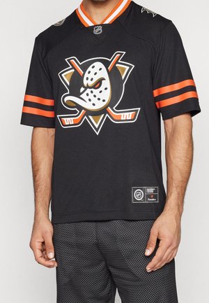 Homme portant un maillot de hockey noir des Anaheim Ducks avec des bandes orange sur les manches et un logo d’équipe représentant un masque de canard en colère avec des crosses de hockey croisées.