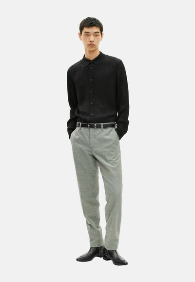 Maglietta nera a maniche lunghe con un motivo sottile, abbinata a pantaloni a scacchi grigi chiari e stivali di pelle nera. Cintura con fibbia in argento.