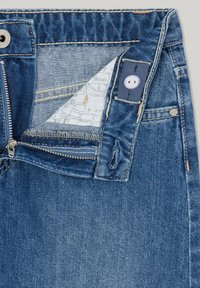 Denim jeans with a blue wash, featuring a zip fly, button closure, and a patterned inner lining. Visible stitching and pockets are included.