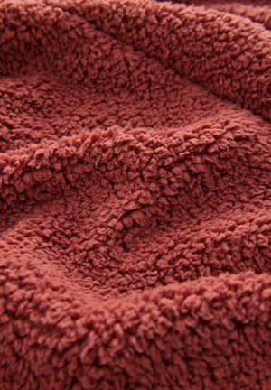 Rjavkasta plišasta odeja z teksturiranim, puhastim površjem; mehak material z izstopajočimi vlakni, ki ustvarjajo prijeten, vabljiv videz.