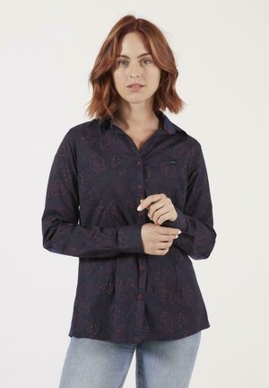 Chemise boutonnée bleu marine avec un motif floral dans des teintes plus foncées, manches longues et un col contrasté. Tissu au toucher lisse et coupe ajustée.