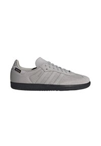 Zapatilla deportiva de ante gris y tejido con suela de goma negra, con tres rayas, cordones en la parte delantera y detalles de marca en el talón.