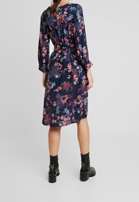 Marinblå blommig klänning med långa ärmar, midjeband och ett subtilt prickmönster. Kombineras med svarta ankelboots och en figursydd siluett.