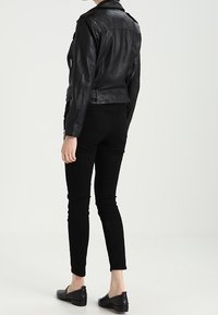 Schwarze Leder-Motorradjacke mit tailliertem Schnitt, sichtbaren Nähten und Reißverschlusstaschen, getragen mit schwarzen Slim-Fit-Hosen und flachen Schuhen.