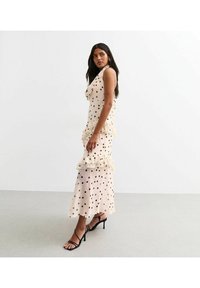 Polka dot dress in cream with black spots, layering ruffles at the hem and bust, paired with black strappy heels, smooth fabric texture.
