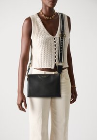Borsa a tracolla in pelle nera con accessori in oro e logo. Design piatto, tracolla regolabile con nome del marchio in caratteri bianchi.