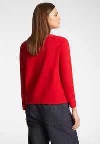 Maglione rosso lavorato a maglia con maniche lunghe, scollatura a girocollo, orlo a coste e una texture liscia, abbinato a pantaloni in denim scuri.