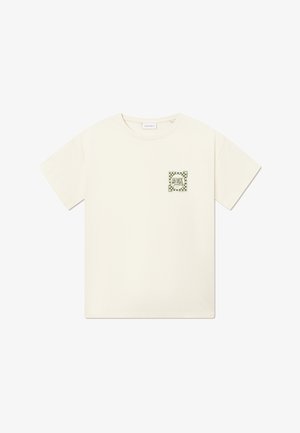 Krém színű pamutszabású póló, válltól válig bő szabással. Bal mellkason zöld kockás logóval ellátott folt. Rövid ujjú és kerek nyakú.