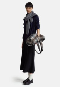 Granatowy dzianinowy sweter, szary prążkowany szal, czarna spódnica, czarne buty oraz kraciasta torba w odcieniach brązu i szarości. Pionowe paski i miękka tekstura.