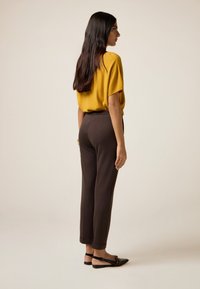 Haut jaune à manches courtes, pantalon brun fuselé et sandales plates noires. Textures lisses, coupe décontractée, avec une silhouette relaxée.