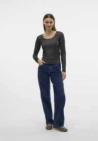 Zwarte geribbelde top met lange mouwen en een ronde hals, gecombineerd met blauwe brede jeans, gedragen met een paar bruine sneakers. Effen achtergrond.