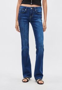 Dżinsy z szerokimi nogawkami w kolorze niebieskim, z pasem o średnim stanie, pięcioma kieszeniami i kontrastowym przeszyciem. Tekstura jest gładka z delikatnym połyskiem.