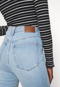 Person som bär ljusblå högmidjade jeans med bakfickor och en svartvit randig långärmad topp.