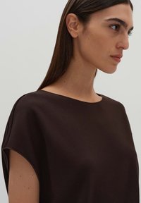 Top marrone a maniche corte con scollatura ampia e vestibilità rilassata, realizzato in tessuto morbido. Design pulito, minimalista e senza decorazioni.