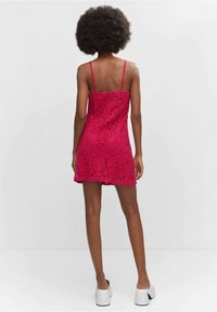 Robe en dentelle fuchsia avec un corsage ajusté, des bretelles spaghetti et un ourlet évasé. Présente un motif floral en découpe.