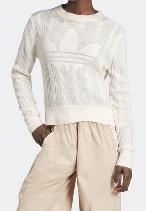 Cream knitted sweater with a textured pattern and a large, tonal logo on the front. Ribbed cuffs and waistband, worn with light beige pants.