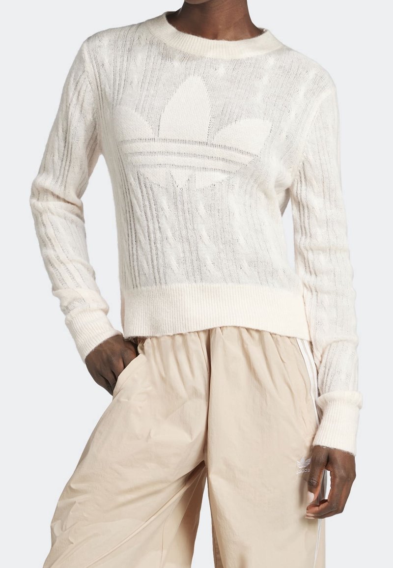 Suéter de punto crema con un patrón texturizado y un gran logo tonal en la parte delantera. Puños y cinturilla acanalados, combinado con pantalones beige claros.