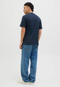 Tricou navy cu guler rotund, mâneci scurte, asociat cu blugi din denim deschis la culoare, cu croială lejeră. Bumbac fin, design casual cu o potrivire relaxată.