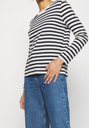 Schwarz-weiß gestreiftes Langarmshirt mit Rundhalsausschnitt; aus weichem Stoff; kombiniert mit mittelblauen High-Waist-Jeans.