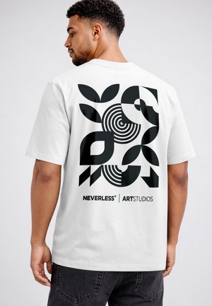 Man wearing a white t-shirt with abstract black geometric shapes and text "NEVERLESS ARTSTUDIOS" on the back, facing away.