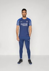 Mornarsko plavi sportski komplet koji se sastoji od majice kratkih rukava i hlača uskog kroja. Ima plave detalje i logotip. Izrađen od prozračnog materijala.