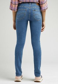 Skarpa blå denimjeans med en texturerad yta, femficksdesign och hög midja, i kombination med ljusa casual skor.