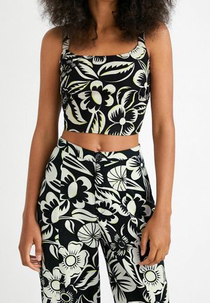 Mujer vistiendo un crop top a juego en negro y blanco con estampado floral y pantalones de talle alto con grandes patrones de flores y hojas.