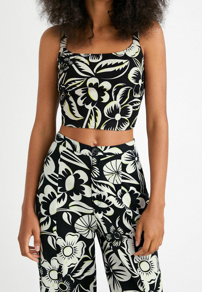 Femme portant un crop top assorti à imprimé floral noir et blanc et un pantalon taille haute avec de grands motifs de fleurs et de feuilles.