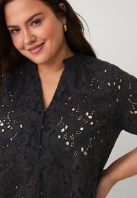 Blusa nera ricamata con intricati motivi floreali, maniche corte, colletto rialzato e bottoni sul davanti.