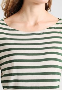 Green and beige striped top with a wide neckline. Soft fabric with a smooth texture, featuring contrasting stripes in horizontal alignment.