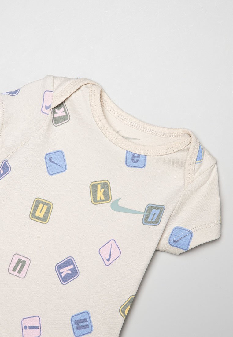 Body beige pour bébé à manches courtes, décoré de blocs colorés présentant des lettres et des logos Nike swoosh.
