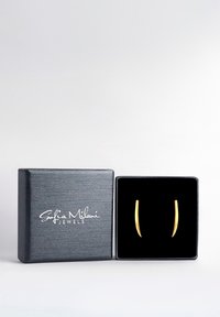Guldtonade örhängen med en slank, cylindrisk design presenterade i en fyrkantig smyckesask klädd med svart sammet. Asken har en texturerad svart yta.