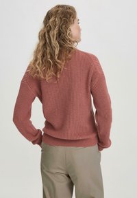 Rosa gestrickter Pullover mit strukturiertem Muster, gerippten Bündchen und Saum, kombiniert mit hellbeigen Hosen. Sicht von hinten.