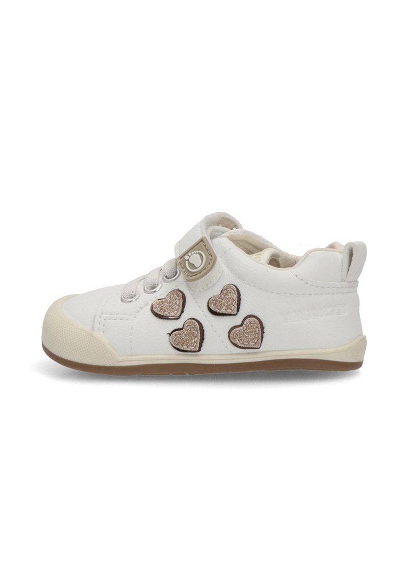 Zapatillas blancas para niño pequeño con suela beige, cuatro parches brillantes en forma de corazón y una correa de Velcro con un ícono de huella.