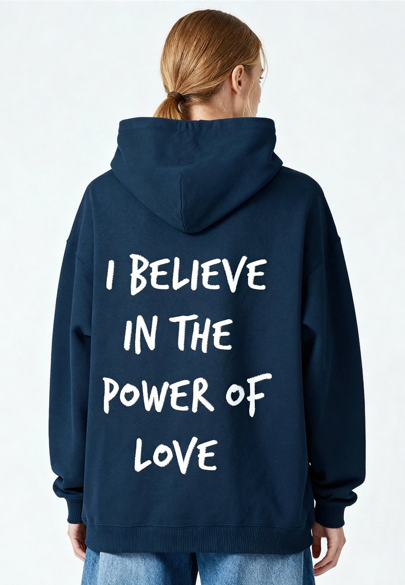 Sweat à capuche bleu marine à coupe ample, avec une poche kangourou et un texte blanc au dos indiquant "JE CROIS EN LA PUISSANCE DE L'AMOUR."