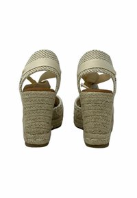 Sandalias de cuña beige con parte superior trenzada, correa ajustable y detalle texturizado elevado en la suela. Parte trasera cerrada con diseño de talón abierto.