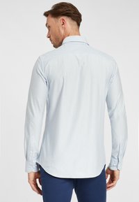 Camicia a maniche lunghe a righe blu chiaro e bianche con colletto a punta, orlo curvo e polsini con bottoni, realizzata in tessuto morbido.