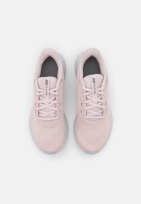 Chaussures de sport rose clair avec une tige en maille, des lacets plats et une semelle intérieure grise texturée. Semelle extérieure en caoutchouc transparent avec des accents bleus. Marque Nike visible.