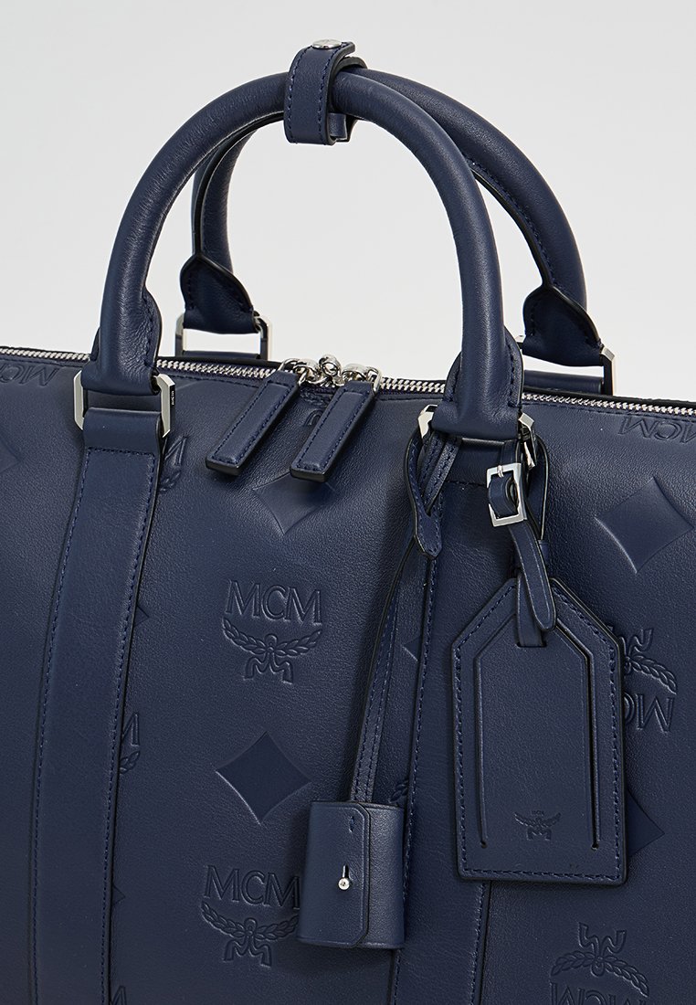 Tiefblaue Lederhandtasche mit geprägtem Logo, doppelten Obergriffen, Reißverschluss und einem Gepäckanhänger mit silbernen Hardware-Akzenten.