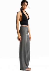 Top court noir à dos nu associé à un pantalon large gris à taille haute. Tissu lisse avec une coupe ajustée. Le modèle se tient dans une pose détendue.