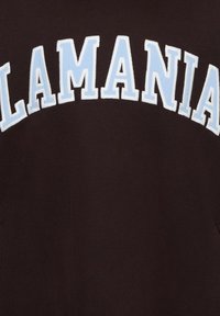 Hanorac negru cu text îndrăzneț alb și albastru deschis care formează cuvântul „LAMANIA” într-un design arcuit, confecționat dintr-un material moale cu textură netedă.