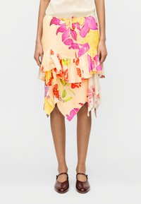 Jupe asymétrique à motif floral couleur pêche, dotée de couches volantes et d'une taille à cordon. Le matériau semble doux et léger.