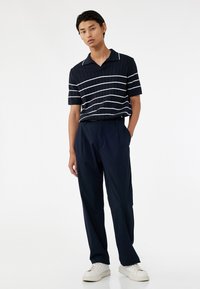 Marineblaues Poloshirt mit weißen Streifen, gerippter Textur und Kragen. Kombiniert mit lockeren marineblauen Hosen und weißen Sneakern.