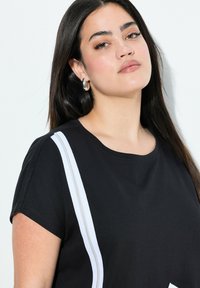 Zwarte t-shirt met korte mouwen, voorzien van witte zijkanten en een ronde hals. Gemaakt van een soepel katoenmateriaal met een relaxte pasvorm.