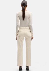 Beżowe spodnie o prostych nogawkach wykonane z denimu, z wysokim stanem i tylnymi kieszeniami. Połączone z lekkim, długim rękawem i czarnymi szpilkami.