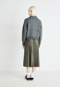 Sweater cinza de malha com um padrão texturizado, combinado com uma saia plissada verde-oliva, meias brancas e sapatos pretos com atacadores.