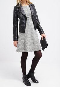 Giacca moto in pelle nera sopra un vestito grigio testurizzato, collant neri e stivaletti. Gli accessori includono una pochette nera.