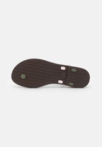 Brown rubber shoe sole with textured pattern, featuring two pink and green accent dots, and indented markings for grip.