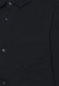 Chemise noire à boutons avec un tissu texturé, col pointu, et une poche poitrine simple, avec un Ourlet droit.