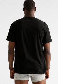 Zwarte katoenen t-shirt met korte mouwen, ronde halslijn en een relaxte pasvorm, van achter bekeken tegen een neutrale achtergrond.